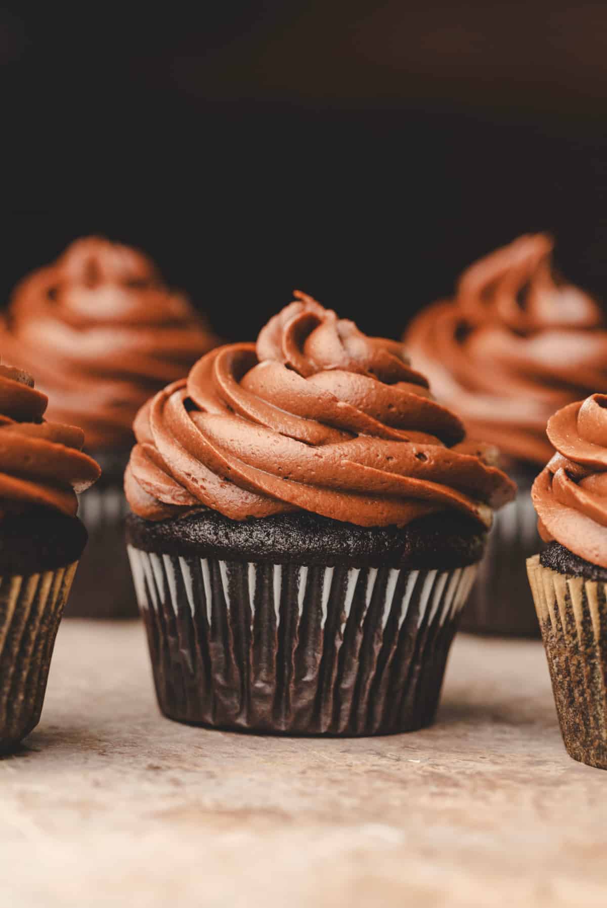 A chocolate cupcake topped with chocolate frosting surrounded by other cupcakes.