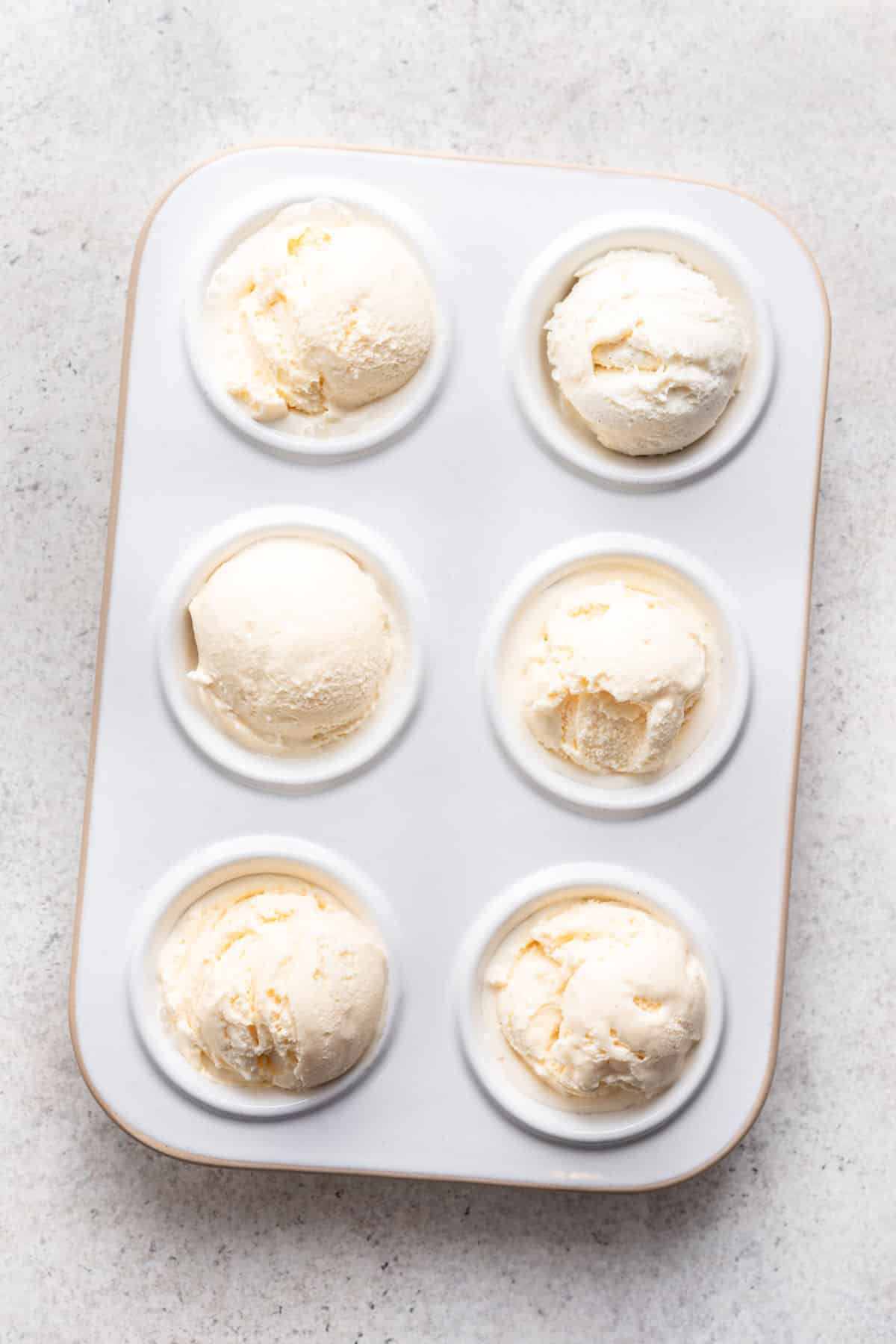 Six scoops of vanilla ice cream in a muffin tin.