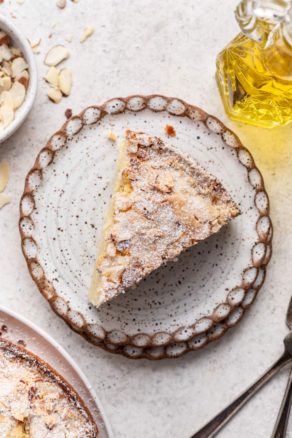 A slice of olive oil cake on a speckled pottery plate. 