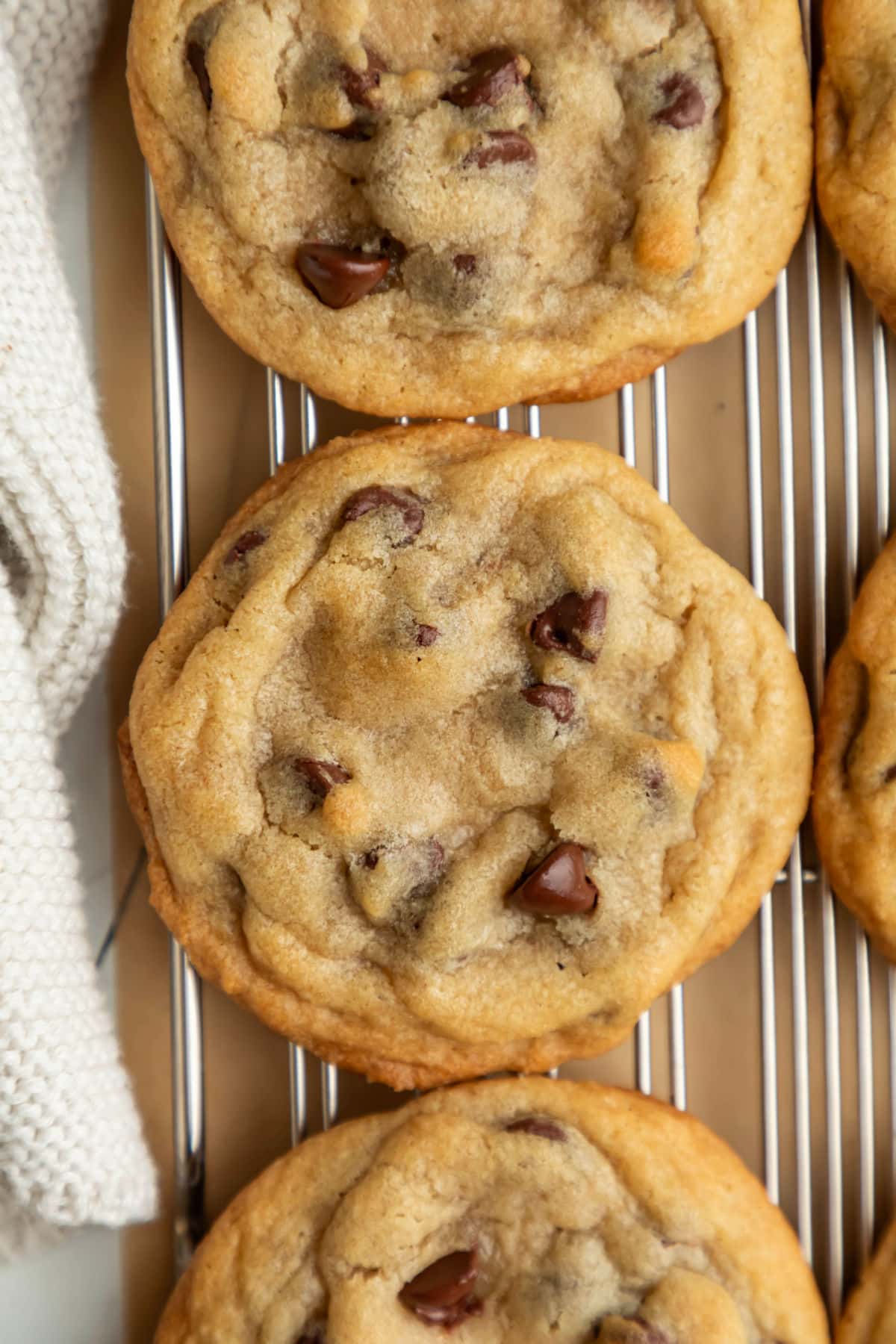 Three bakery style chocolate chip cookies on a wire cooling rack.