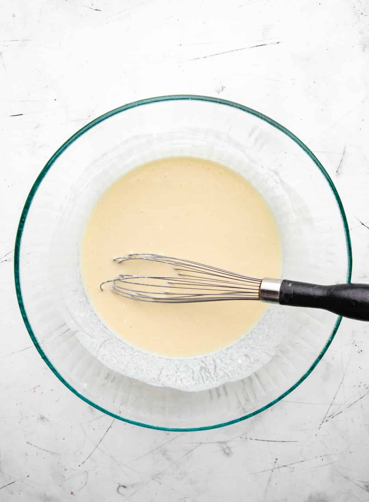 Eggs oil buttermilk and sour cream whisked together in a glass mixing bowl. 