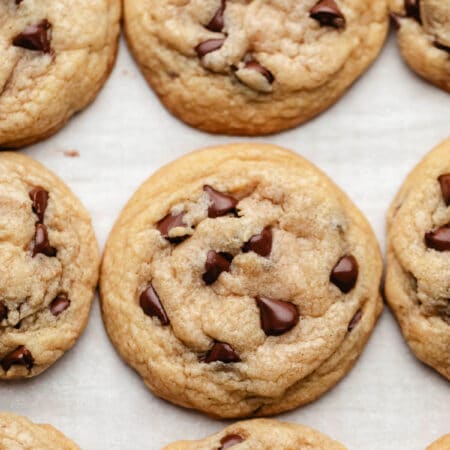 Three rows of chocolate chip cookies on a piece of white parchment paper.