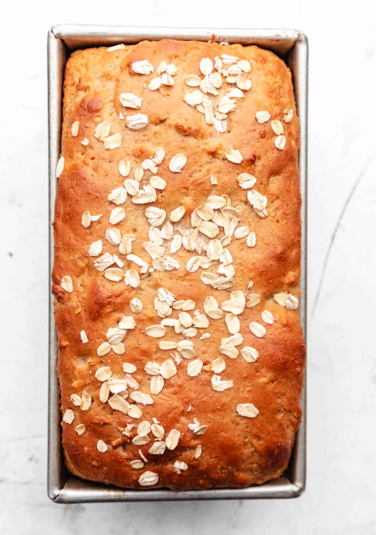 A baked loaf of honey oat bread in a loaf pan.