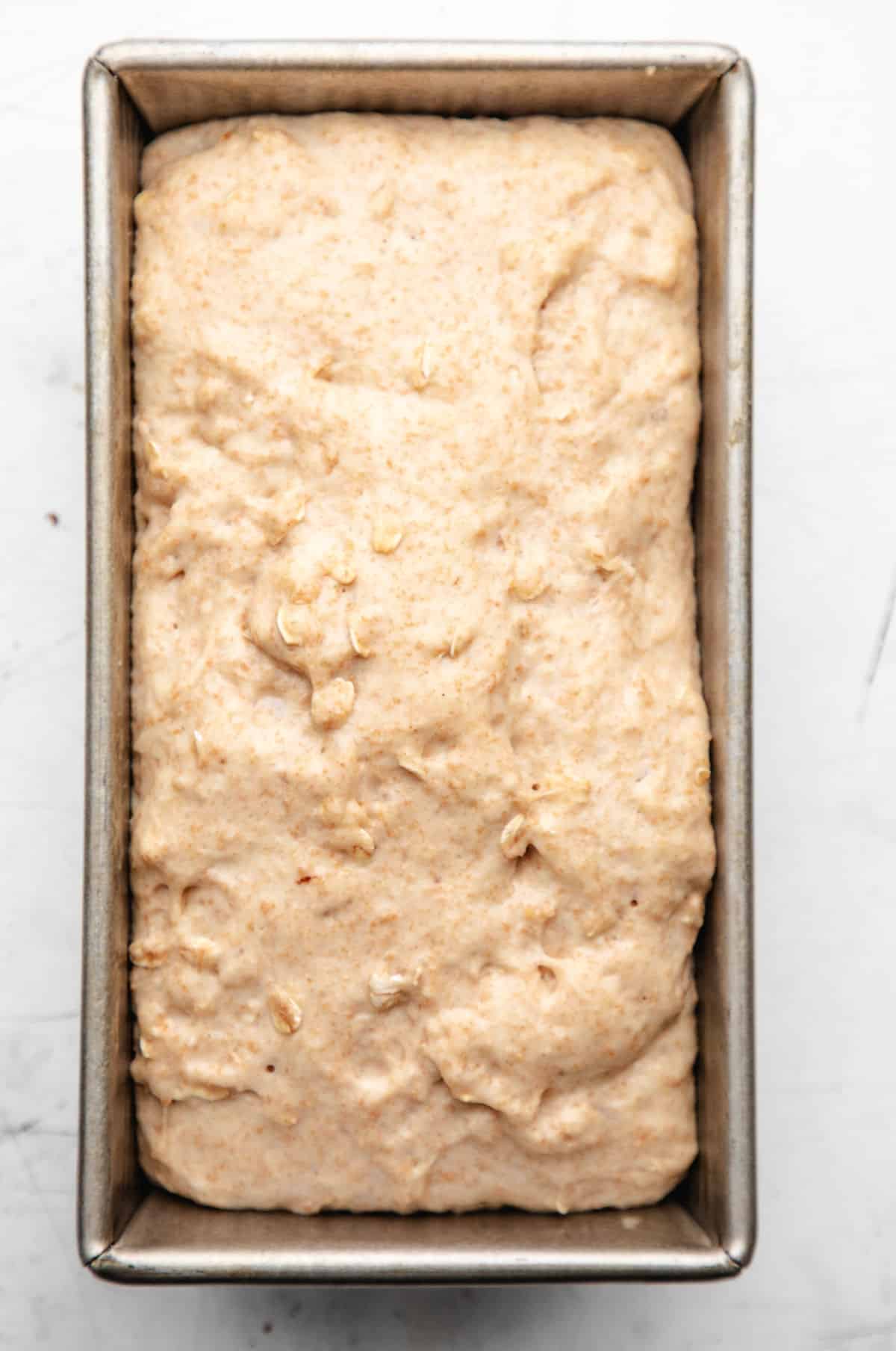 Risen honey oat bread dough in a loaf pan.