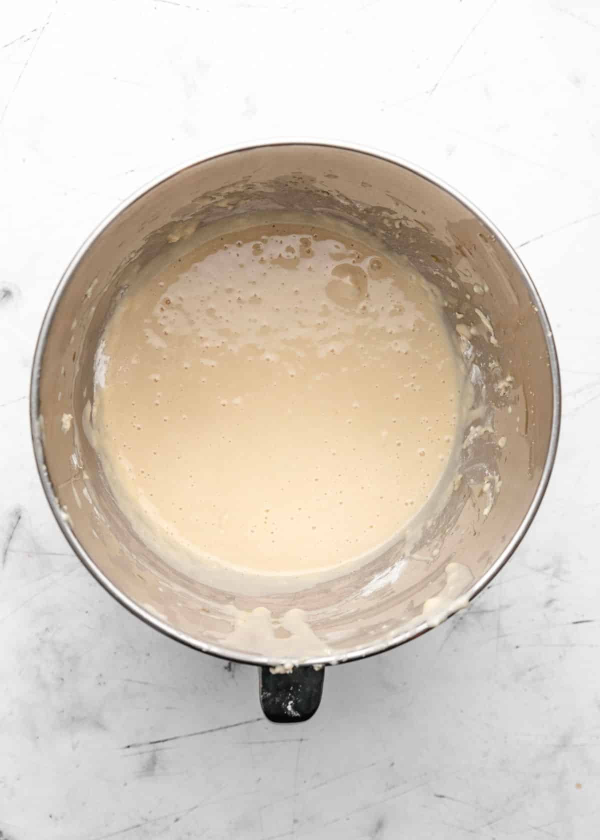 Egg and oil mixed into yeast and milk mixture in a silver mixing bowl. 
