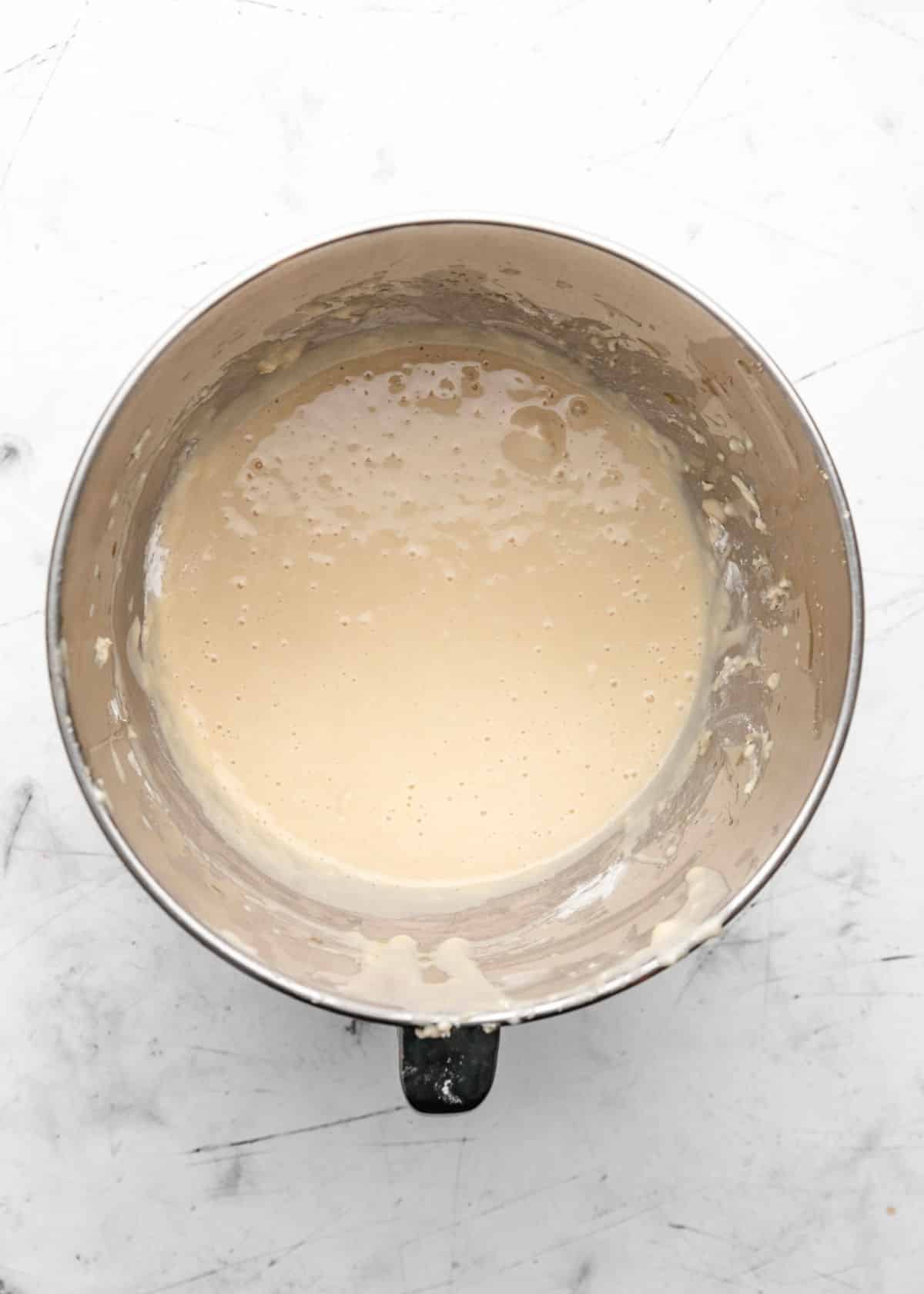 Egg and oil mixed into yeast and milk mixture in a silver mixing bowl.