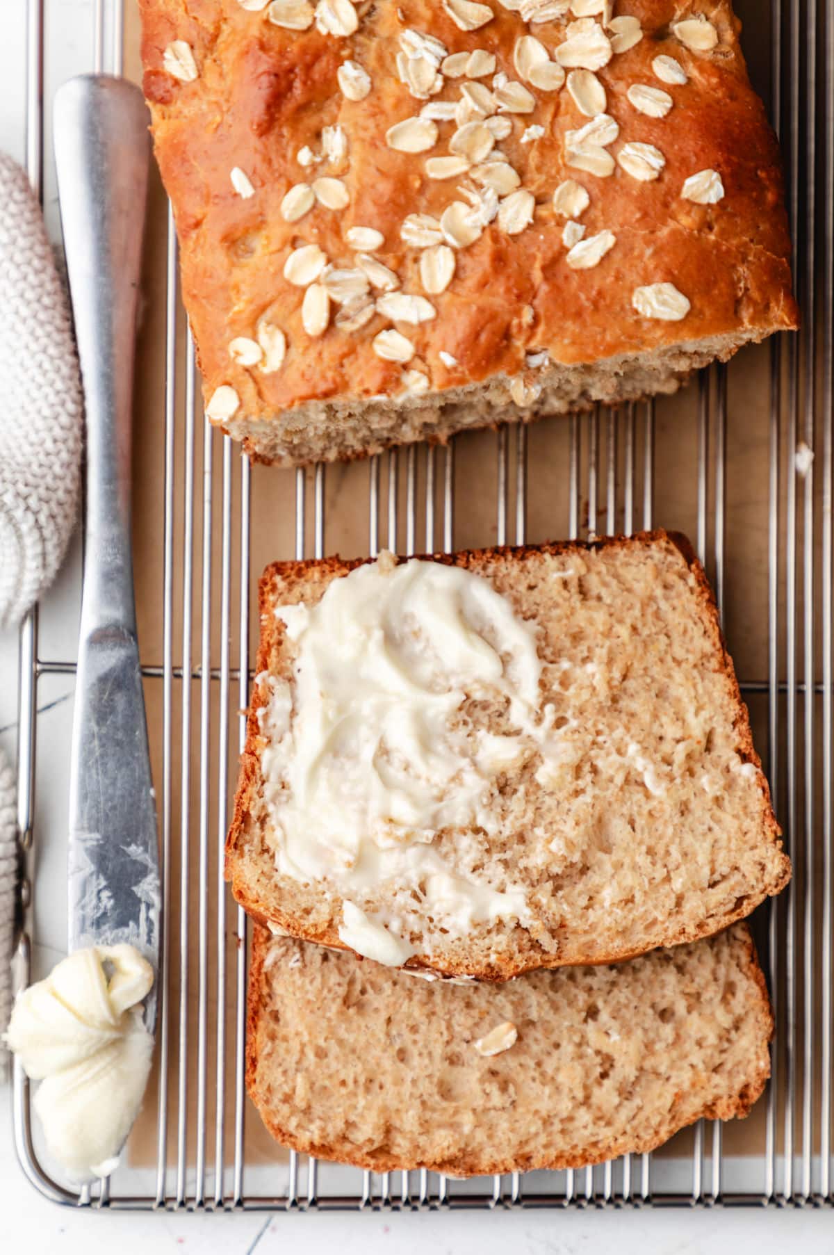 A partially buttered slice of honey oat bread next the loaf.