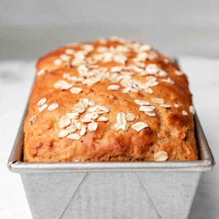 A baked loaf of honey oat bread in a bread pan.