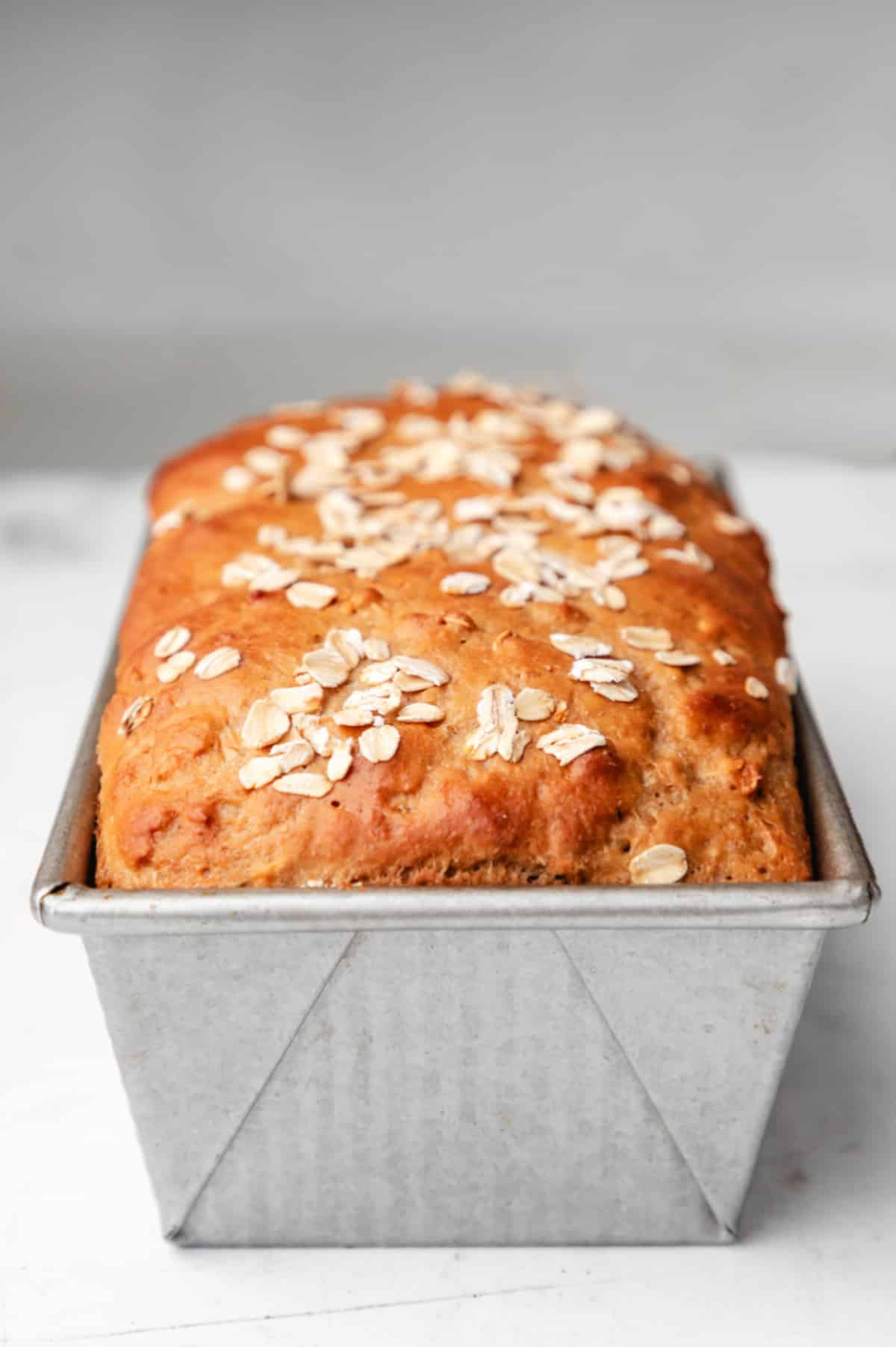 A baked loaf of honey oat bread in a bread pan.