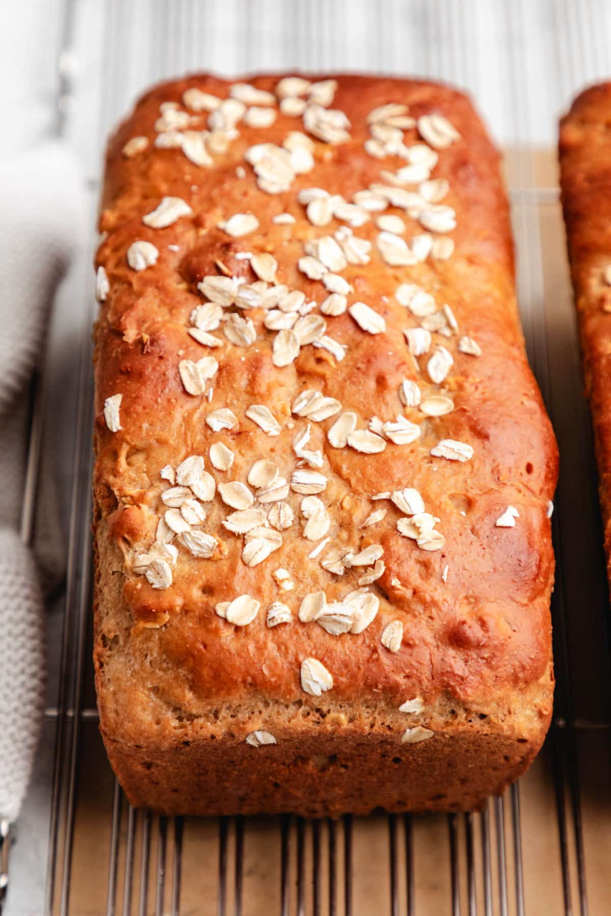 A loaf of honey oat bread on a wire cooling rack next to a knit dish cloth.