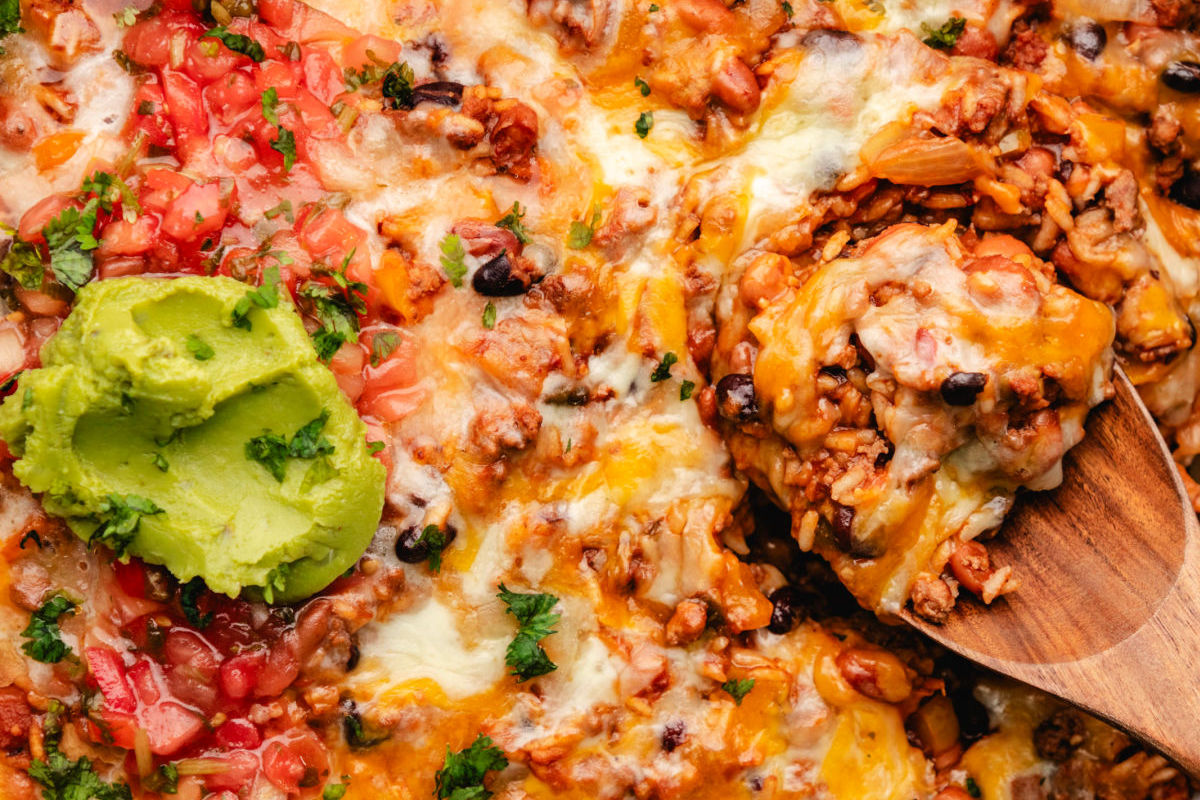 a wooden spoon holding a scoop of Mexican ground beef and rice next to a scoop of guacamole.