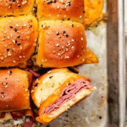 A baked roast beef slider on its side next to more sliders.