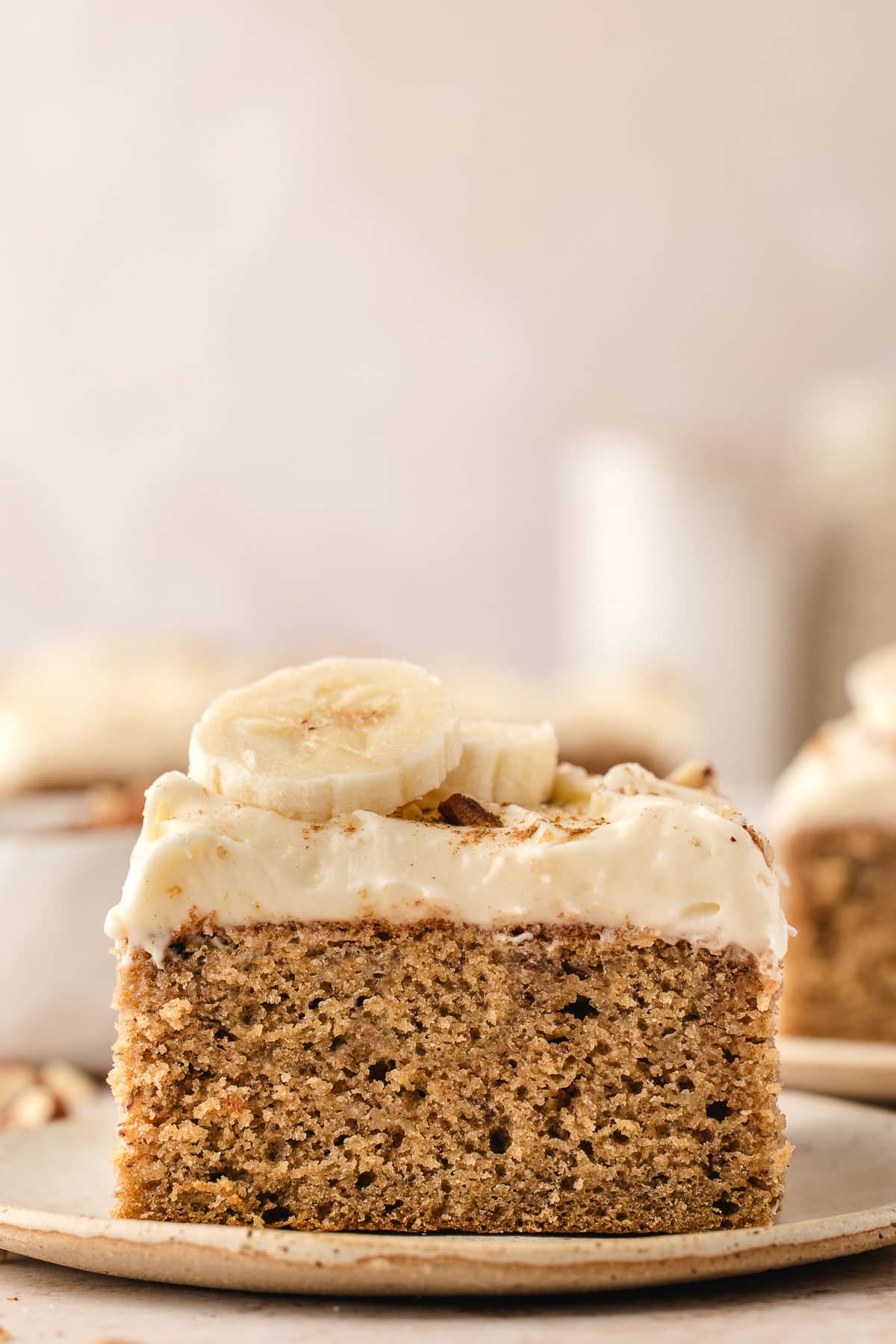 A slice of banana cake topped with cream cheese frosting and slices of fresh banana.