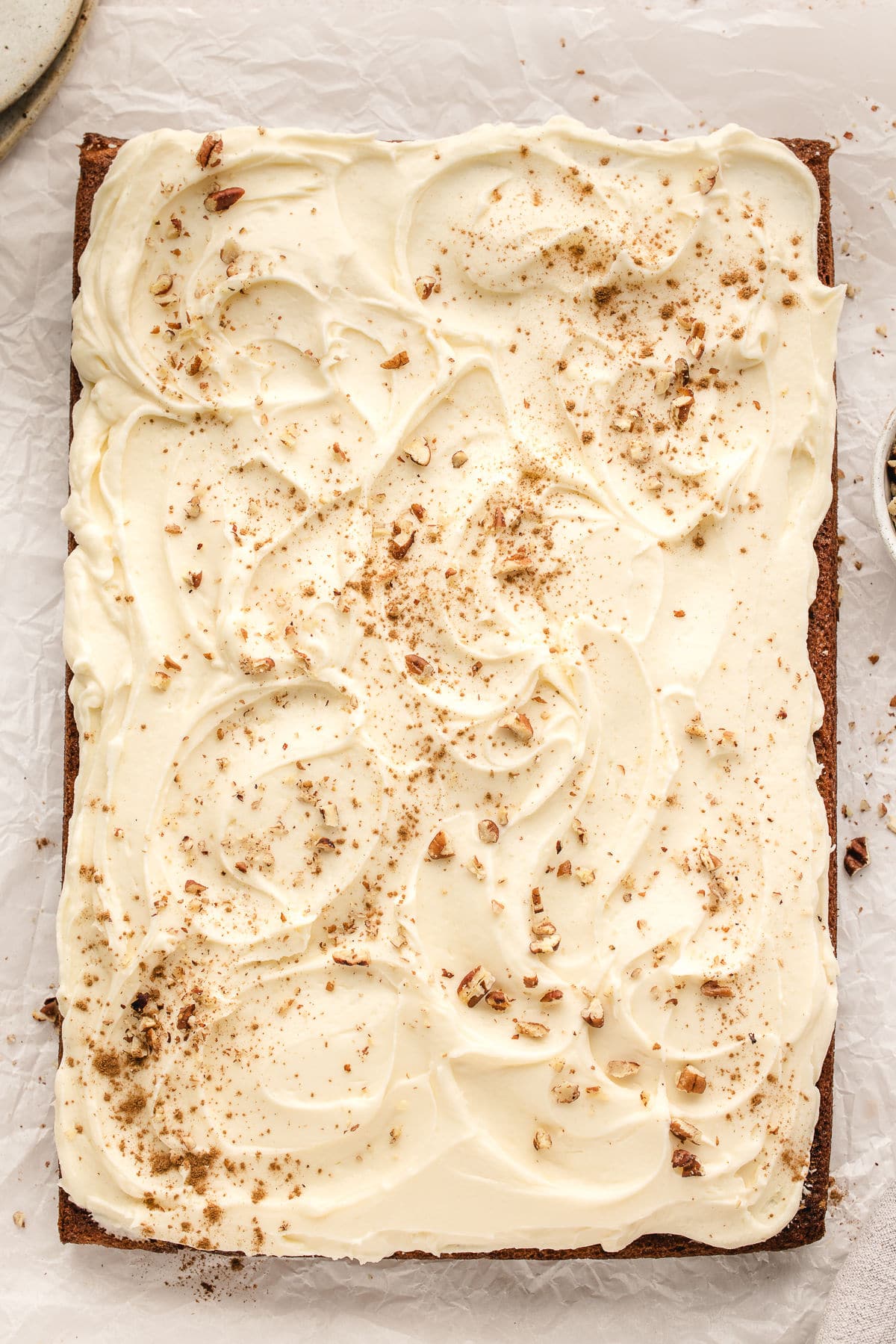 A banana sheet cake topped with cream cheese frosting and a few chopped pecans.
