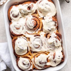 A white pan of baked overnight cinnamon rolls topped with cream cheese frosting.