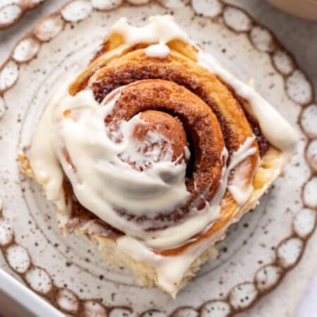 A partially frosted cinnamon roll on a speckled pottery plate.