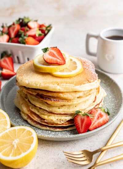 A stack of lemon ricotta pancakes topped with a slice of lemon and half a strawberry.