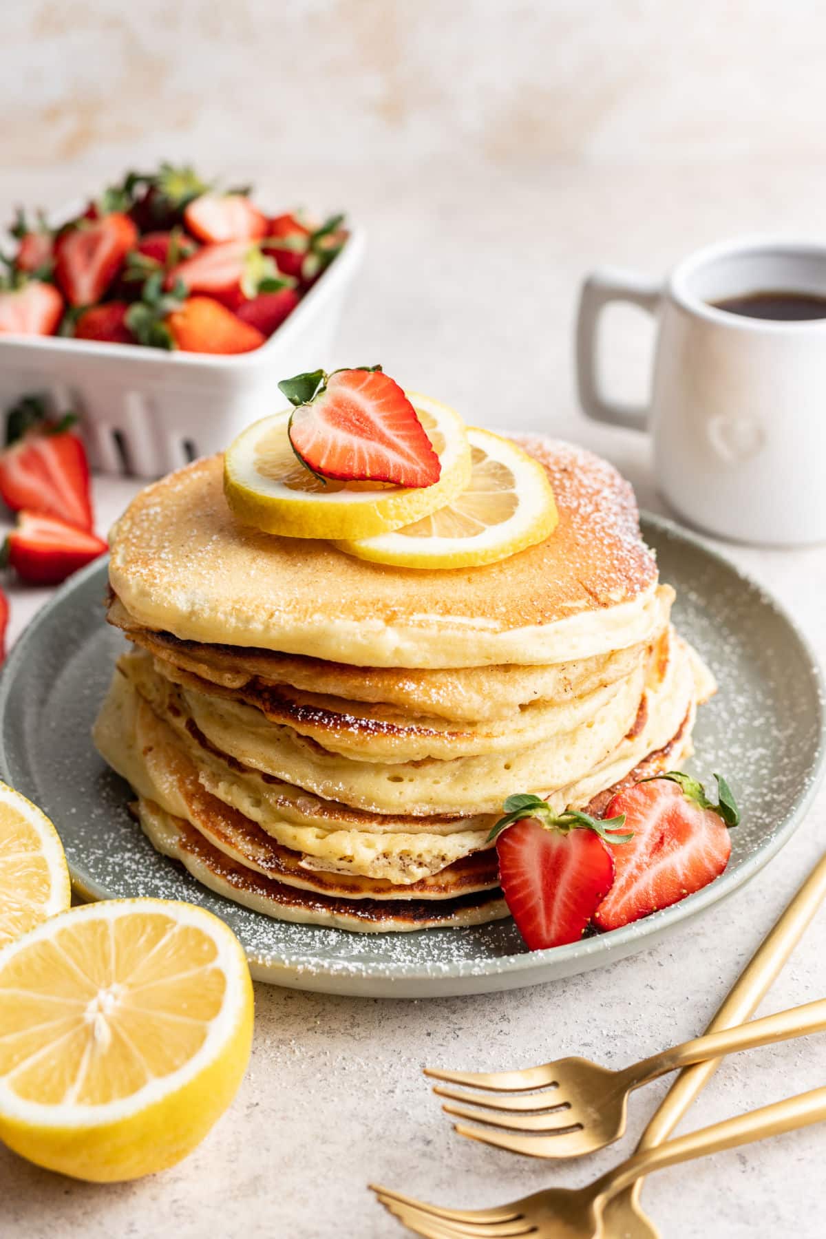 A stack of lemon ricotta pancakes topped with a slice of lemon and half a strawberry.