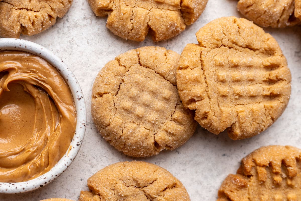 Overlapping peanut butter cookies next to a dish of peanut butter.