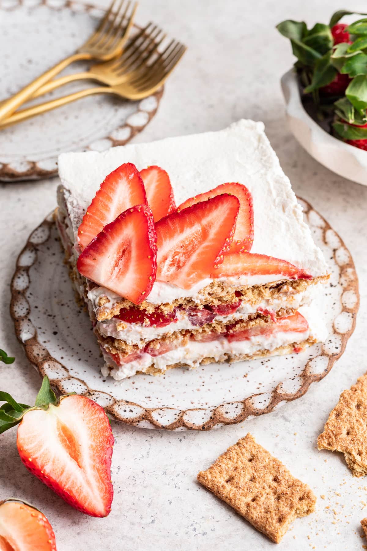 A slice of strawberry icebox cake next to three gold forks. 