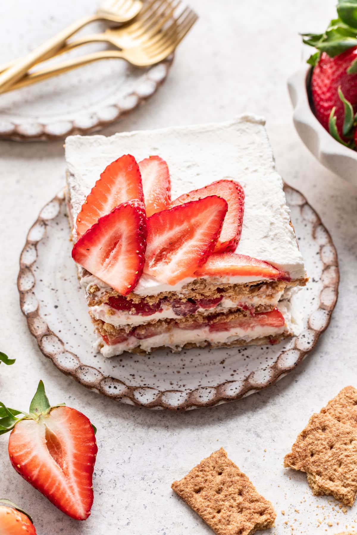 A slice of strawberry icebox cake next to a bowl of fresh strawberries.