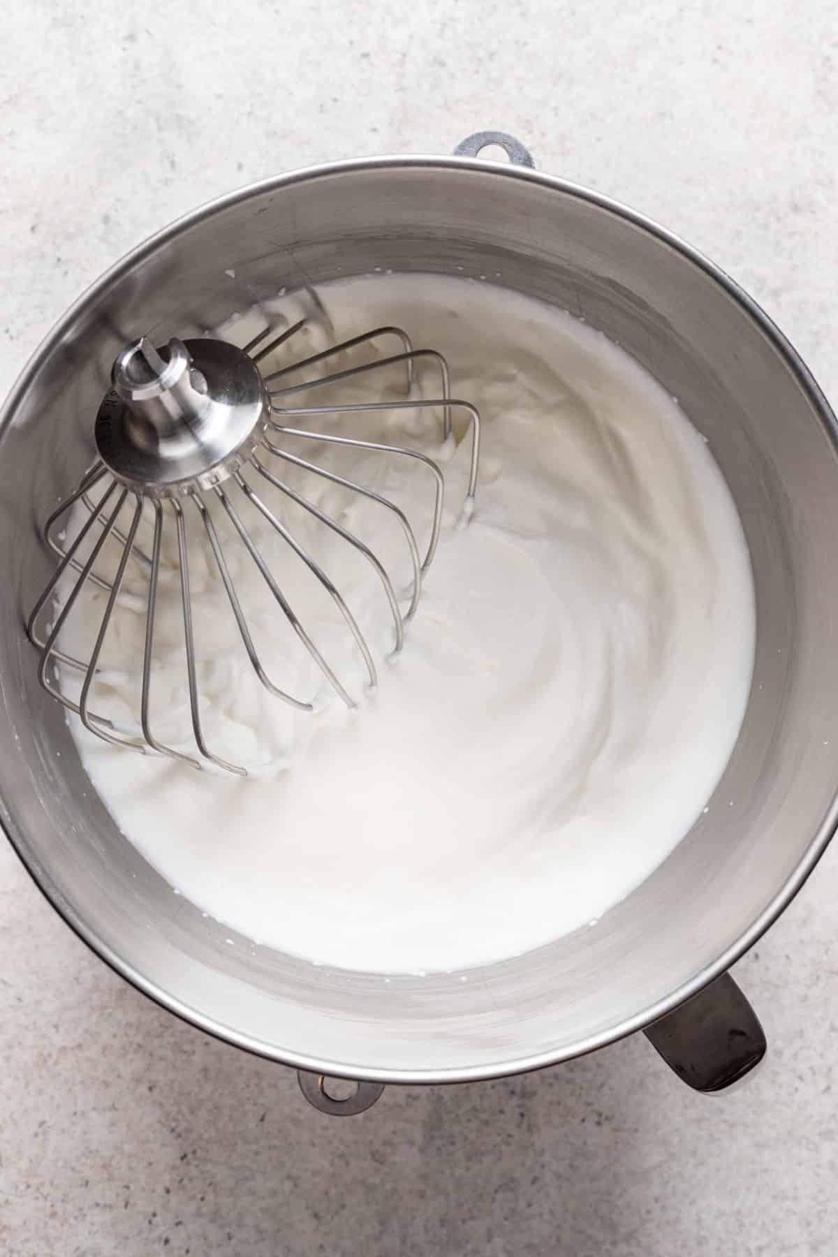 A whisk attachment in a bowl of soft peak whipped cream. 