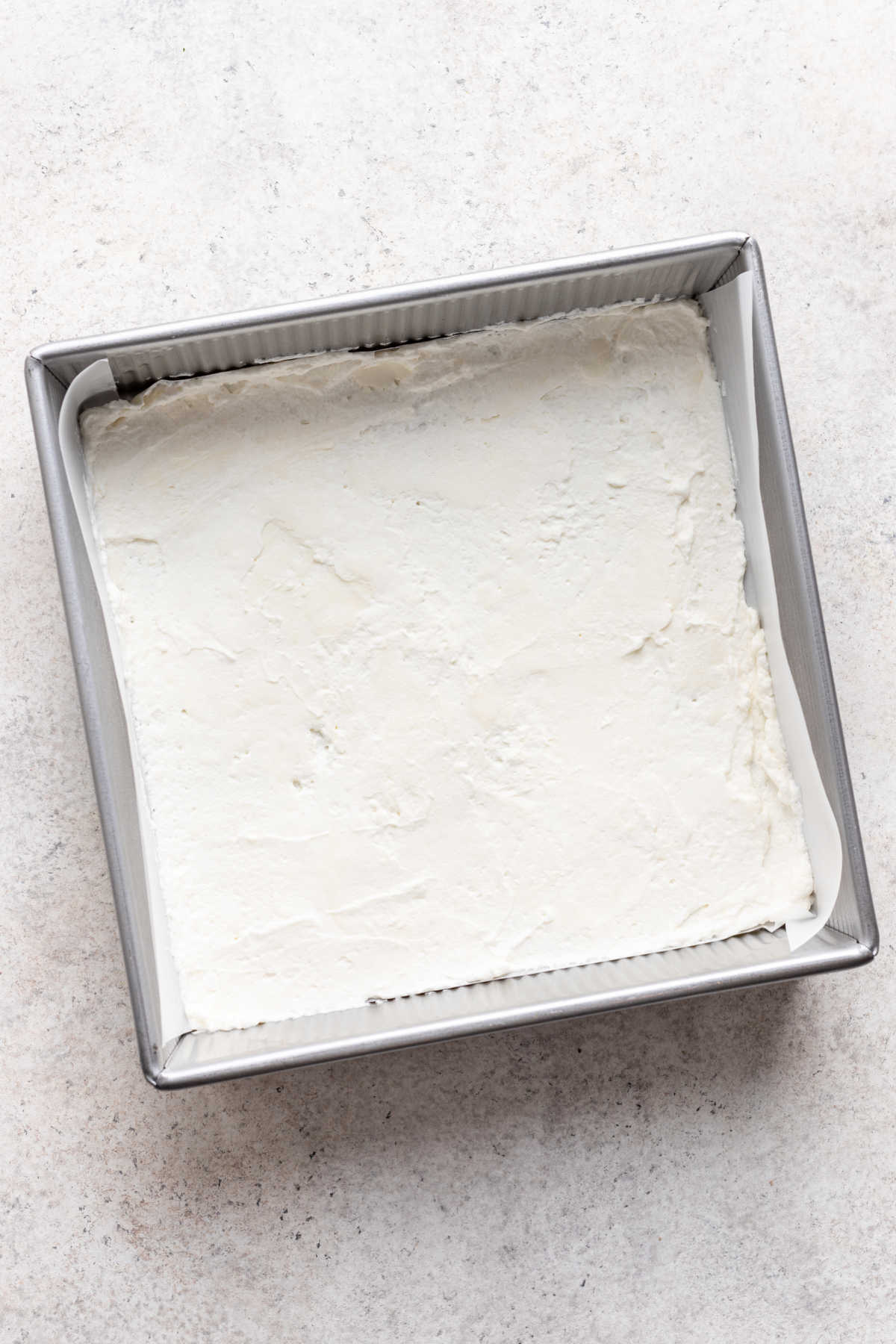 A thin layer of cream cheese whipped cream in the bottom of a pan.