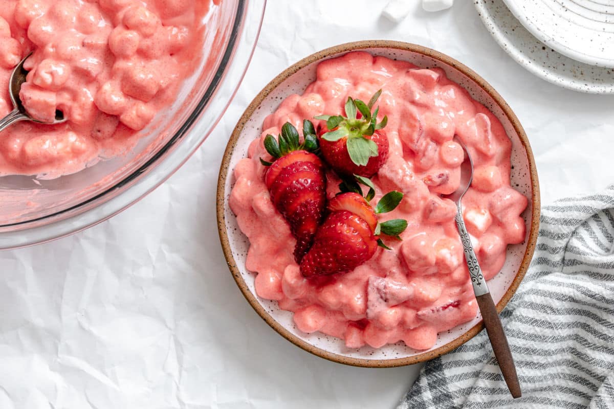 A bowl of strawberry fluff next t to a dish of strawberry fluff with a spoon in it.