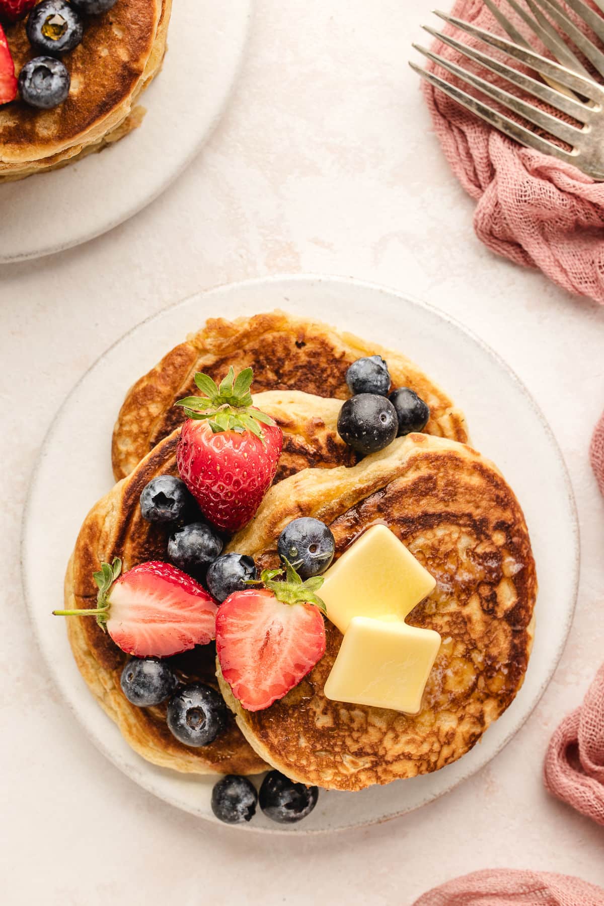 A plate of sweet cream pancakes topped with pats of butter and fresh berries.
