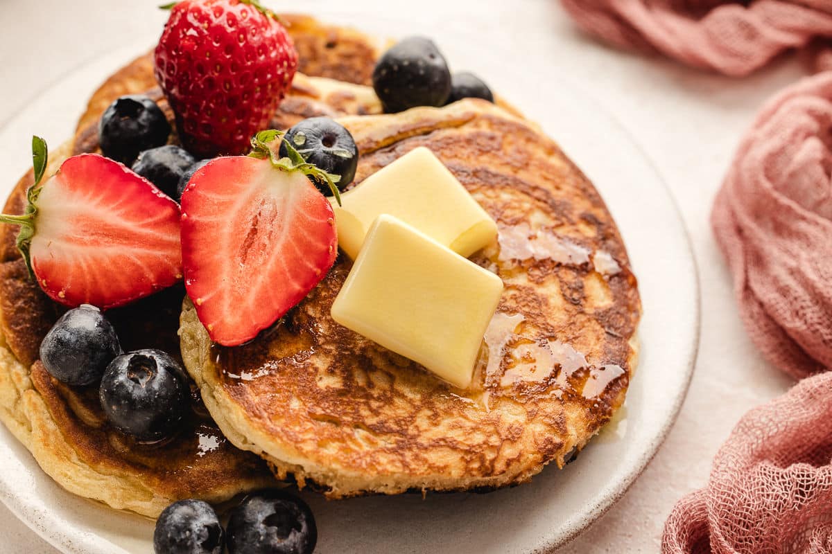 A sweet cream pancake topped with pats of butter, maple syrup, and fresh berries.