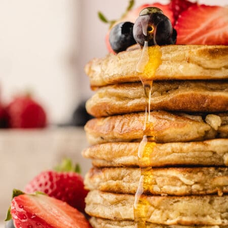 Maple syrup pouring onto a stack of sweet cream pancakes.
