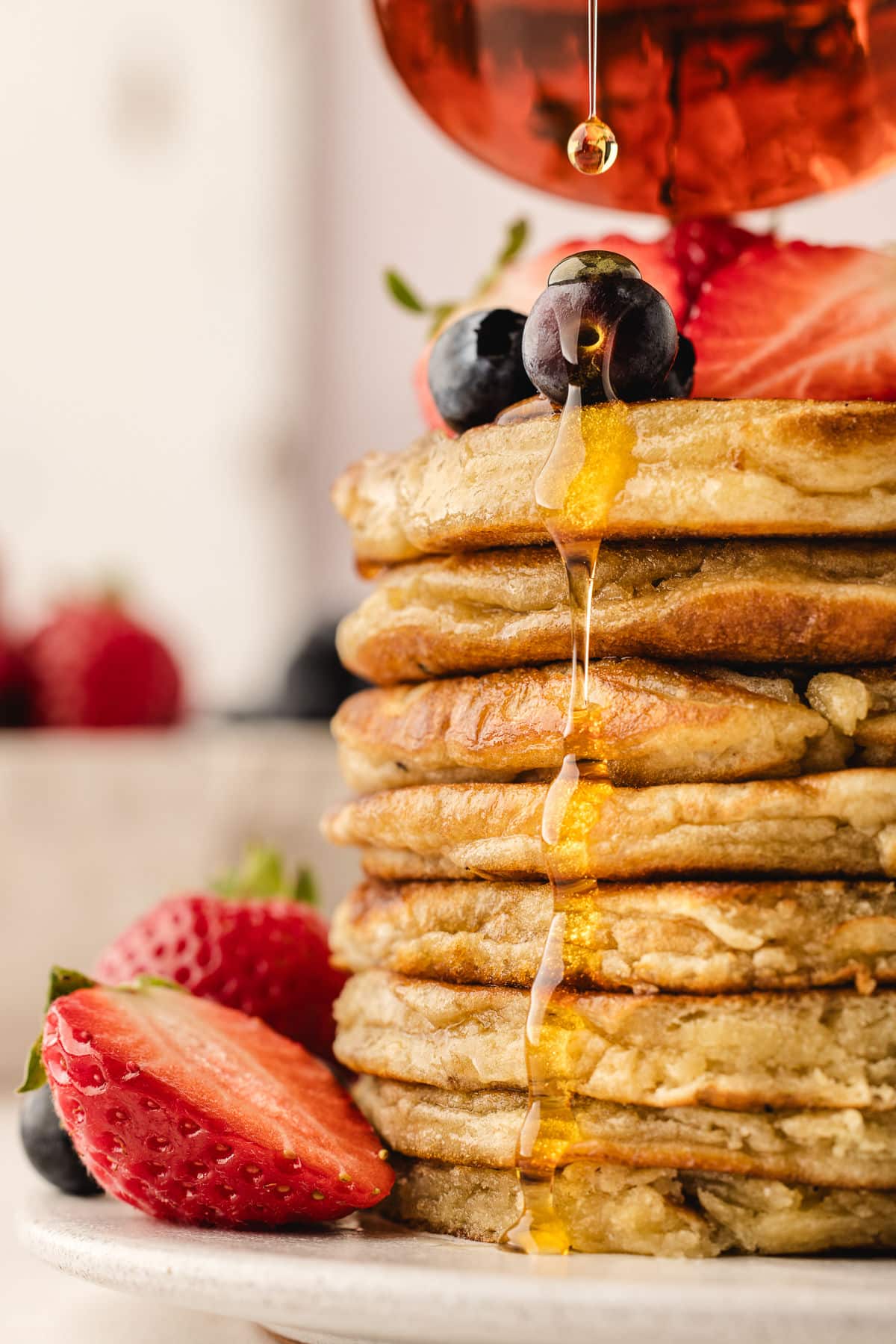 Maple syrup pouring onto a stack of sweet cream pancakes.