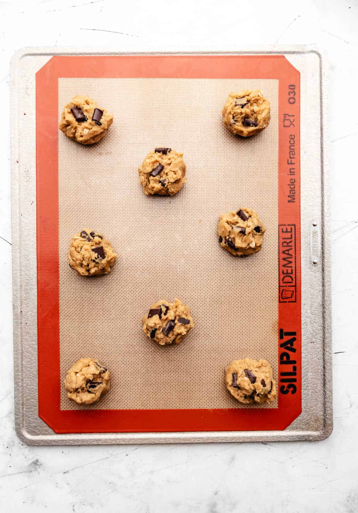 Eight scoops of chocolate chip cookie dough on a baking sheet. 