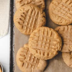 Overlapping peanut butter cookies on a piece of brown parchment paper.