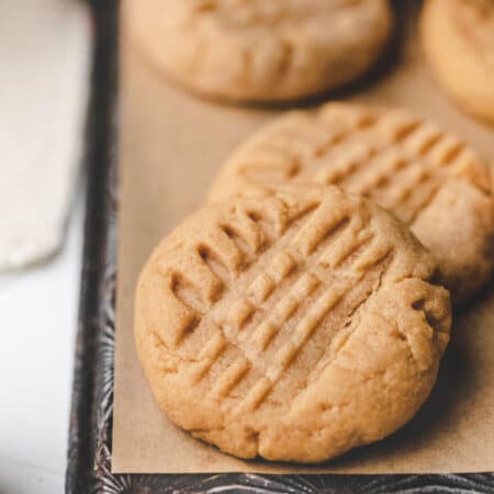 A peanut butter cookie leaning on other cookies on a piece of brown parchment paper.