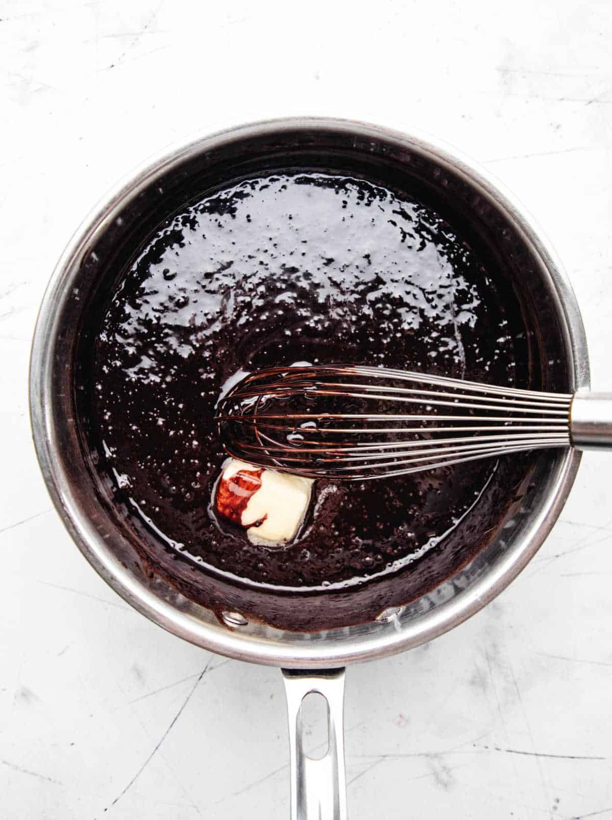 A whisk stirring butter into hot fudge sauce.