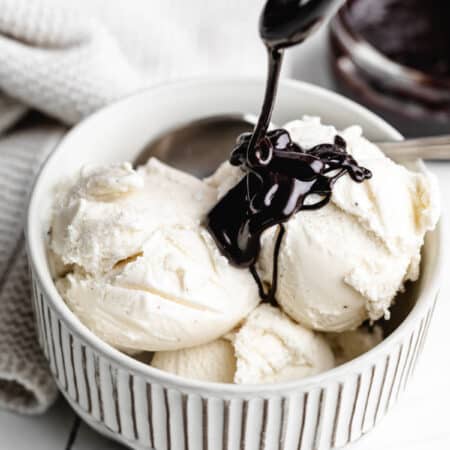 A spoon drizzling hot fudge onto vanilla ice cream.