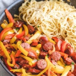 A skillet with kielbasa and peppers and spaghetti.