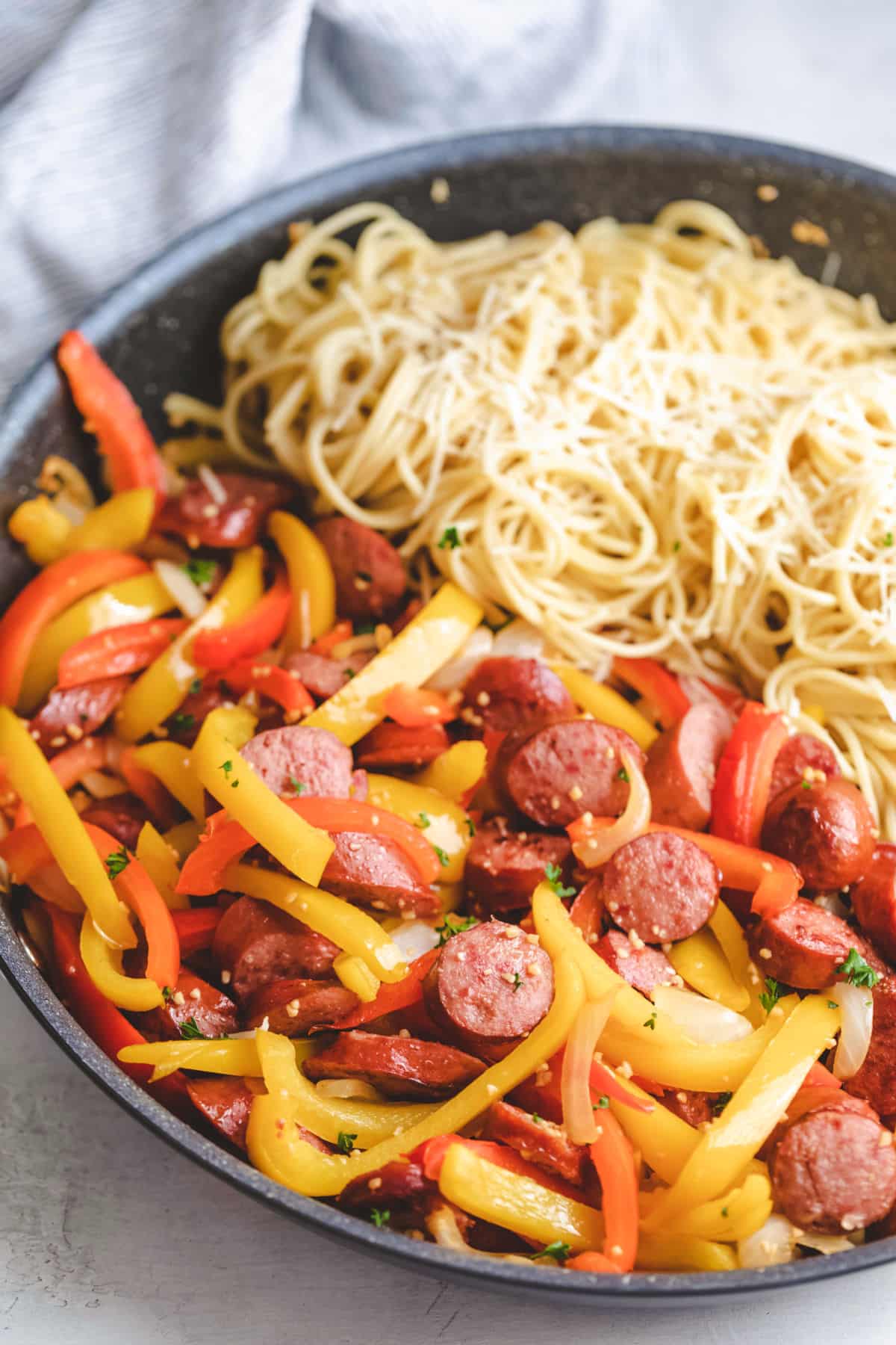 A skillet with kielbasa and peppers and spaghetti.