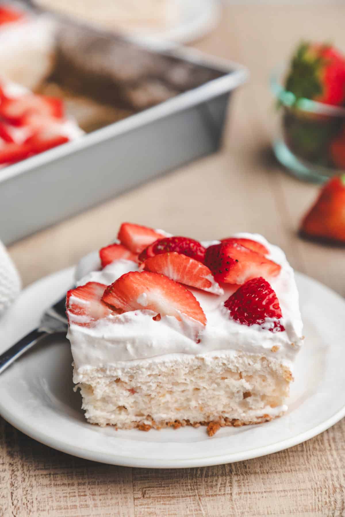 A plate of strawberry yogurt cake next to a bowl of fresh strawberries. 