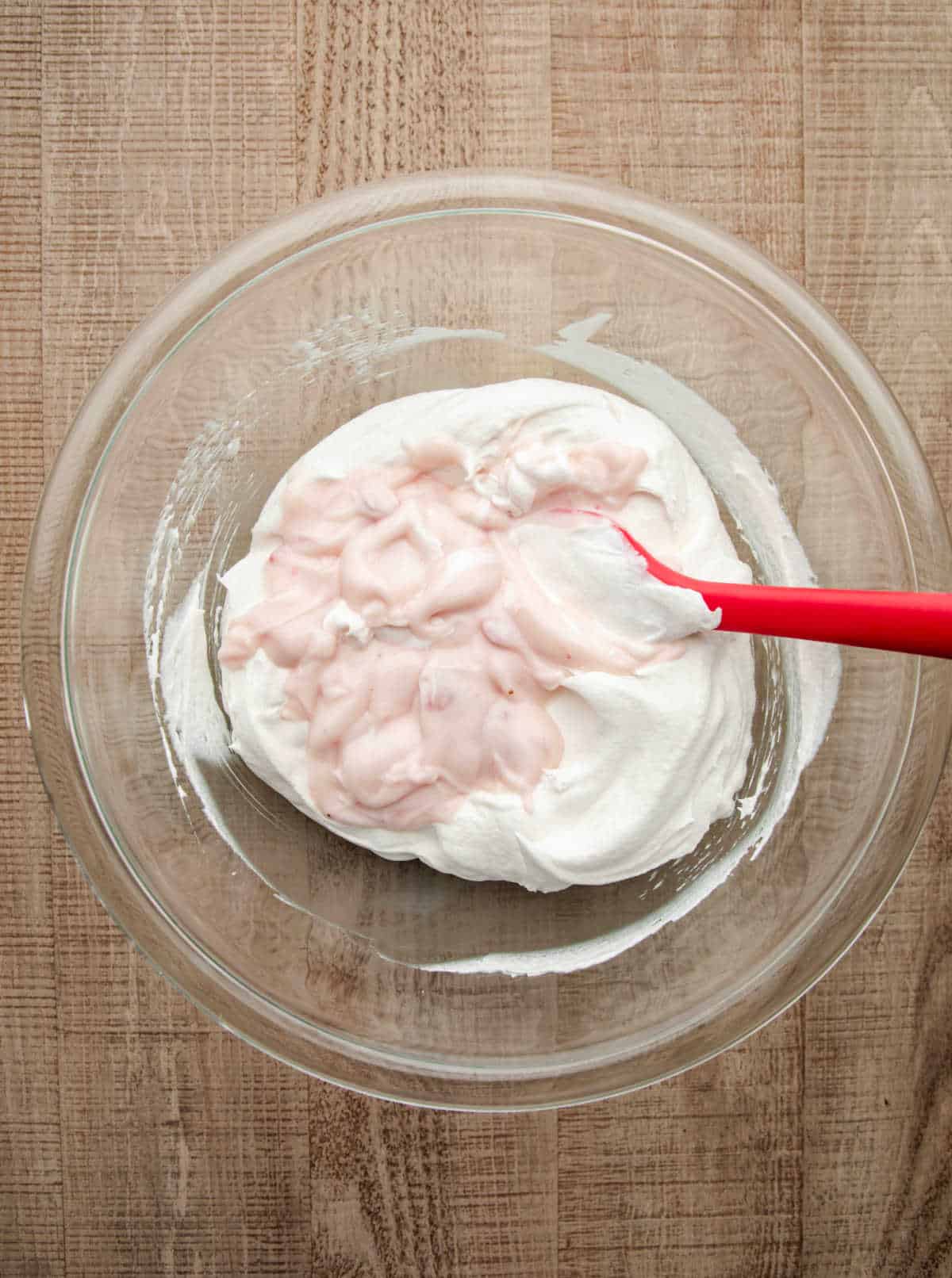 Strawberry yogurt and cool whip in a glass mixing bowl. 