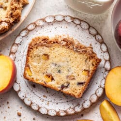 A slice of peach cobbler cake next to fresh sliced peaches.