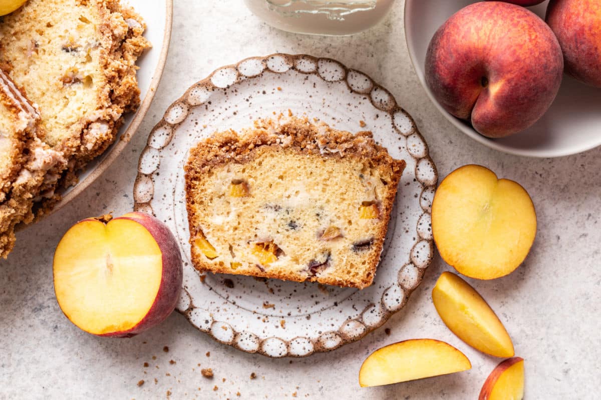 A slice of peach cobbler cake next to the cake and a dish of peaches.