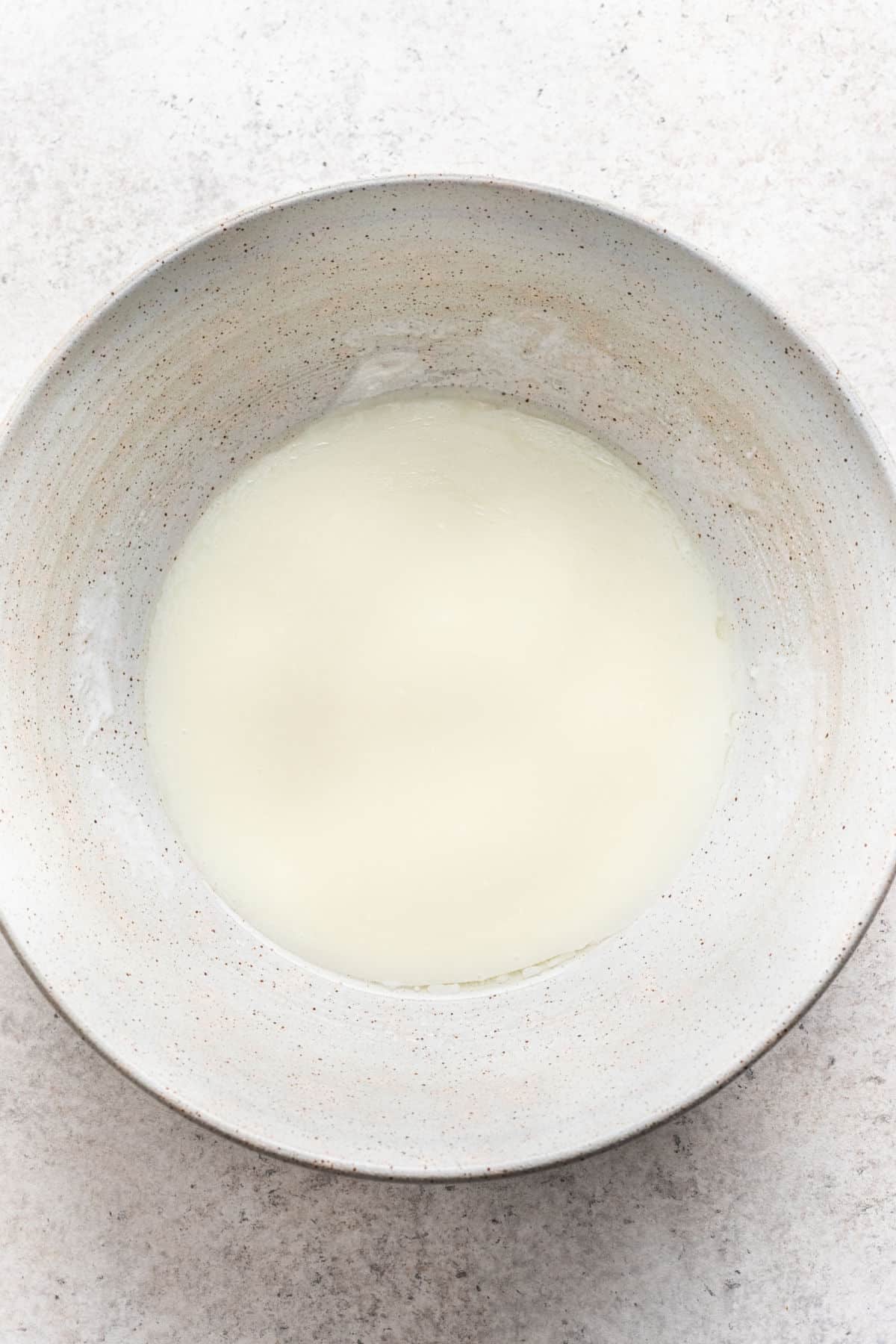 Huile, babeurre, crème aigre et sucre mélangés dans un bol à mélanger blanc.