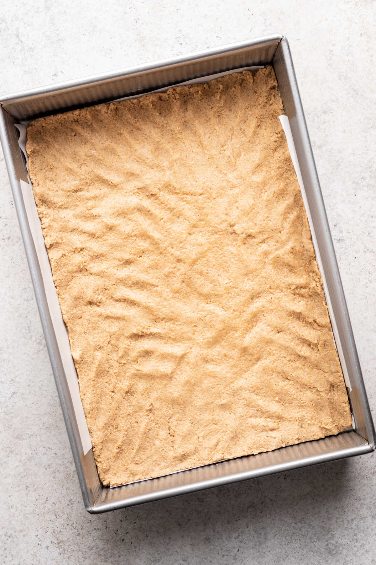 Half of the graham cracker dough pressed into a 9 by 13 pan.