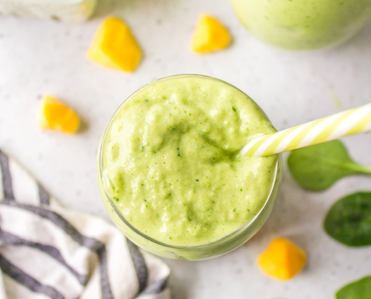 Overhead view of green smoothie with a straw in it.