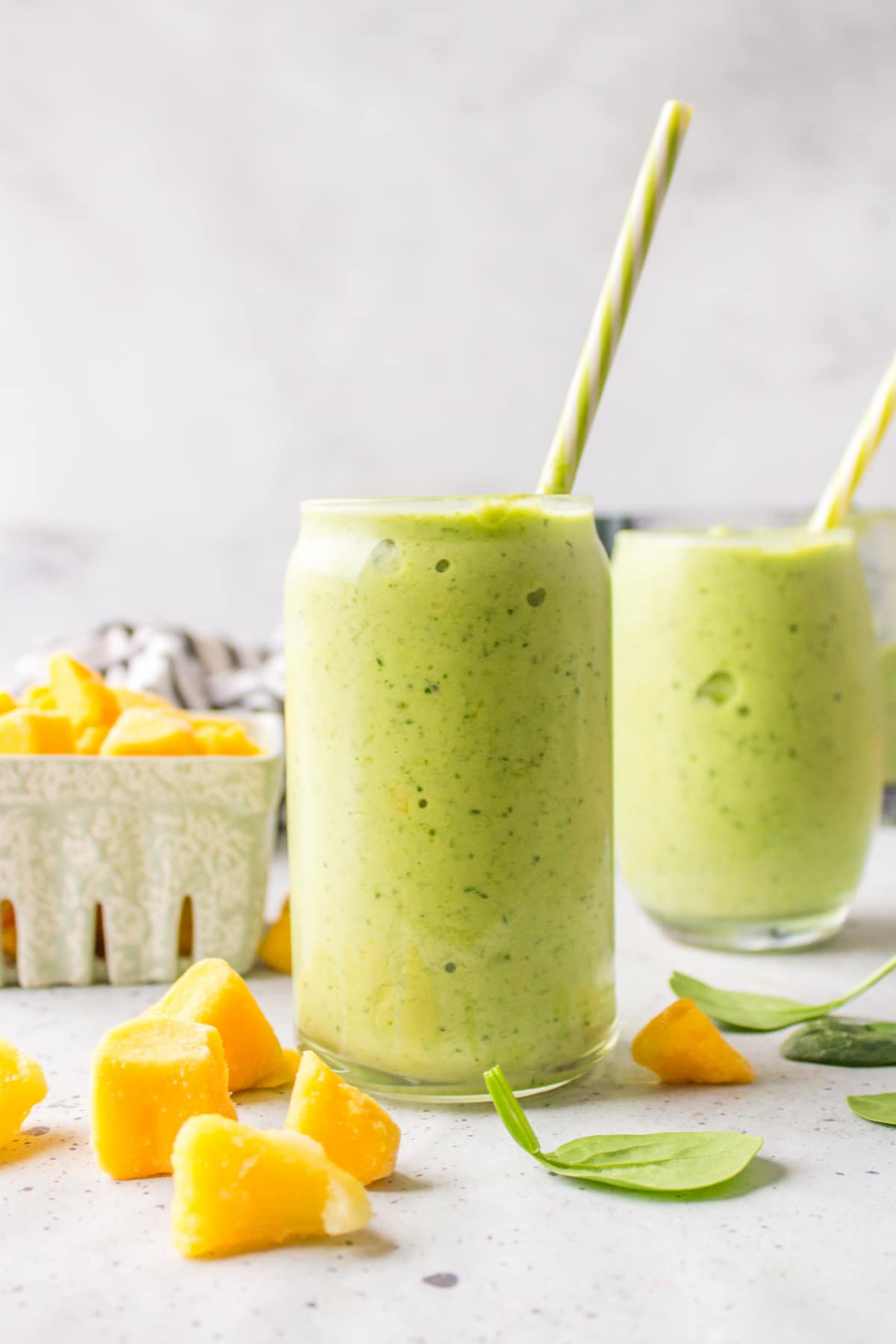 Two glasses of tropical green smoothie next to mango chunks.
