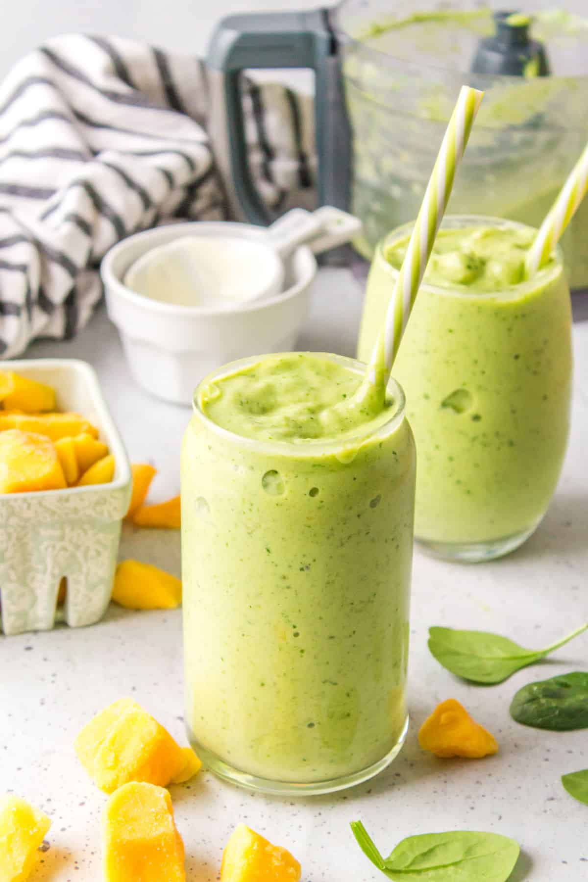 Two glasses of green smoothie with straws in them.