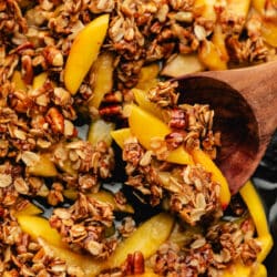 A wooden spoon holding a scoop of peach crisp in a skillet.