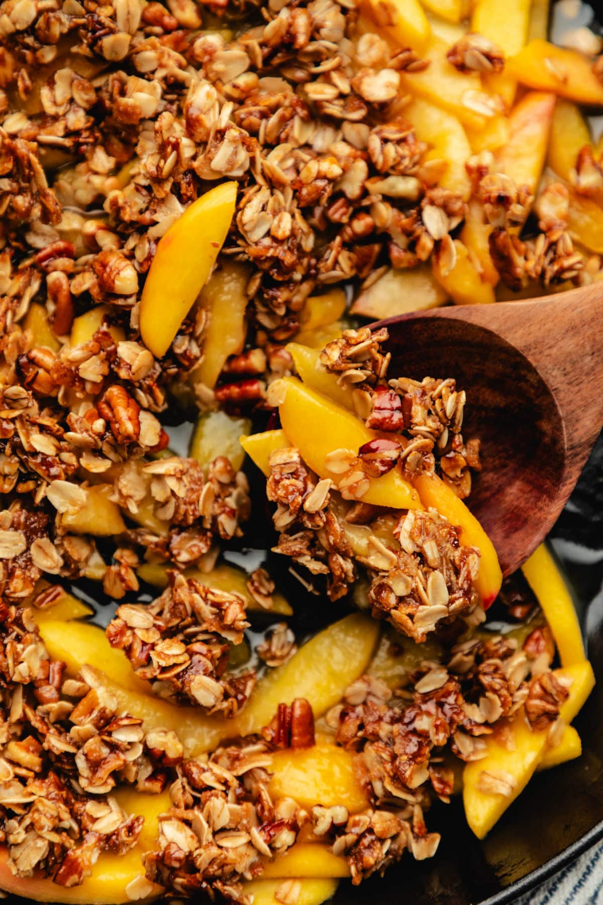 Easy Peach Crisp A wooden spoon holding a scoop of peach crisp in a skillet.